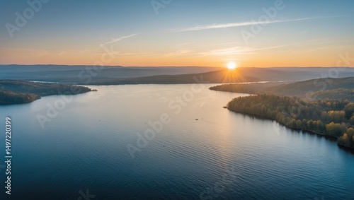 Sunset over a large river or lake with surrounding forested hills.