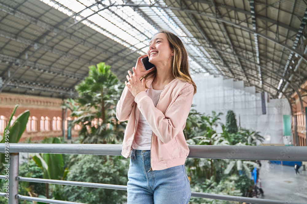 Fototapeta premium Young woman talking on smartphone and gesturing in station