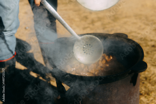 Meat cooking in a large cauldron outdoors over an open fire, a classic outdoor cooking concept for camping and traditional cuisine.