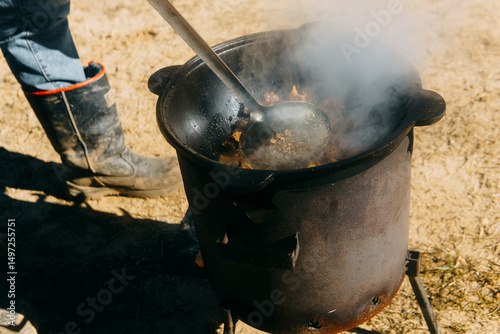 Meat cooking in a large cauldron outdoors over an open fire, a classic outdoor cooking concept for camping and traditional cuisine.