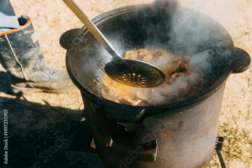 Meat cooking in a large cauldron outdoors over an open fire, a classic outdoor cooking concept for camping and traditional cuisine.