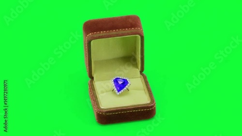 Elegant Engagement: A beautifully crafted sapphire ring, nestled within a rich velvet box, set against a vibrant green background, perfect for proposals and celebrations of love. 
