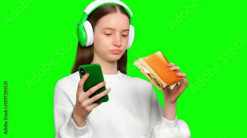 Lunchtime Serenity: A young woman engrossed in her phone, simultaneously enjoying a sandwich and listening to music through her headphones.