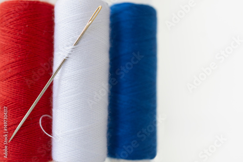 Studio shot of needle and spools of red, white and blue thread