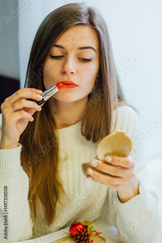 Woman applying red lipstick while looking in a compact mirror. Makeup application concept for beauty and cosmetic advertising.