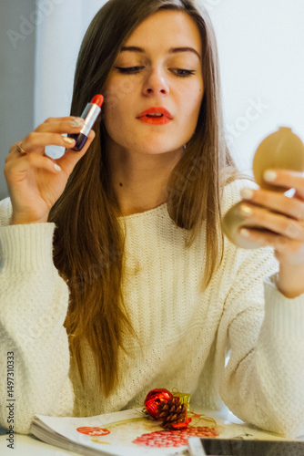 Woman applying red lipstick while looking in a compact mirror. Makeup application concept for beauty and cosmetic advertising.