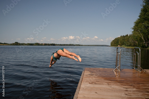 Fit woman diving headfirst from pier into lake. Healthy body, strong motion, natural summer activity.