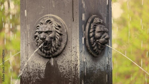 Close Up View Of An Ornate Fountain Featuring Two Lion Head Sculptures From Which Streams Of Water Are Gushing. Classic Architectural Detail In A Park.