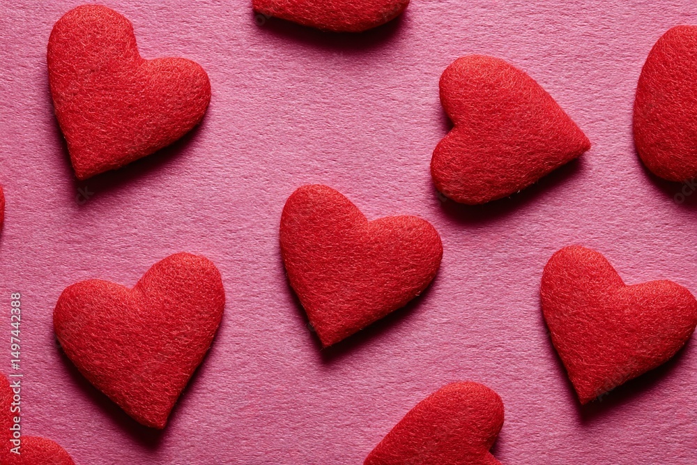Obraz premium Colorful red felt hearts scattered on a vibrant pink surface create a visually appealing backdrop for celebrations and romantic occasions