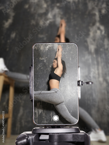 Fitness influencer doing home workout and stretching on yoga mat while live streaming on smartphone. Sporty young woman filming online fitness training for social media followers