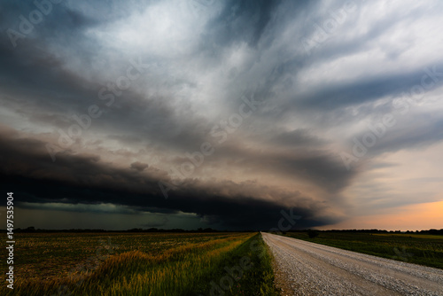 Φωτογραφία A dramatic view of thunderclouds approaching over a deserted road, with heavy shadows stretching across flat farmland under a sky brimming with stormy tension