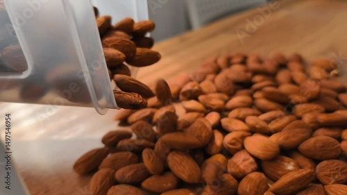 A close-up video shot of sliced almonds slowly pouring onto a wooden table, creating a natural and appetizing pile. 