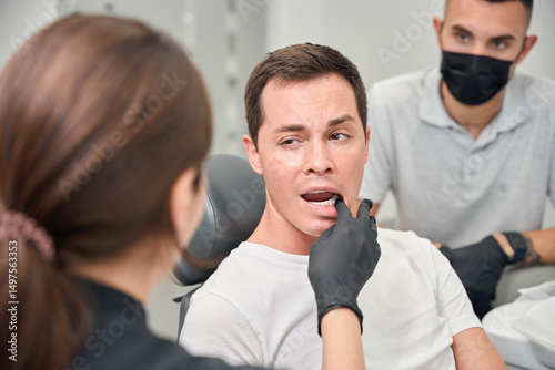 Fotografie Female stomatologist checking loose tooth of male client