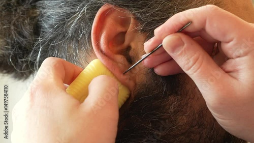 Close-up of a man carefully piercing another person's ear with a sterile needle. A staged procedure using clean instruments. Demonstration of a do-it-yourself ear piercing in a safe home environment