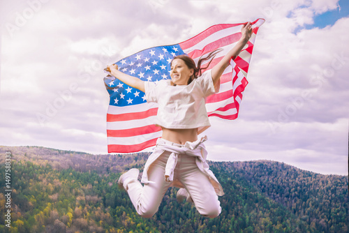 A young woman with an American flag in nature, jumping against the background of mountains. A patriotic holiday. The United States celebrates July 4th. The concept of Independence Day