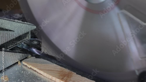 Blade of a miter saw to cut off the edge of a wooden board, close up. Working on a circular saw in a workshop