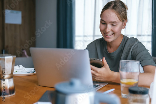 Free Download  Gen Z woman working from home at cozy kitchen table with laptop and phone. Digital nomad lifestyle, mindfulness, remote work, balance, mental calm and modern freelancing - GFXLoad