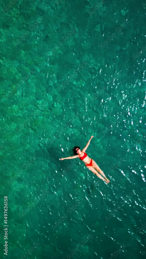Woman in red swimsuit lays on her back in the clear sea, top down view Woman in red swimsuit lays on her back in the clear sea, top down view