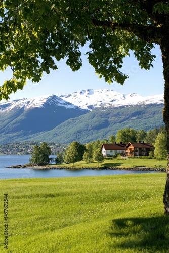A peaceful lakeside house sits on a lush green meadow, with snowy mountains and clear blue skies in the background.