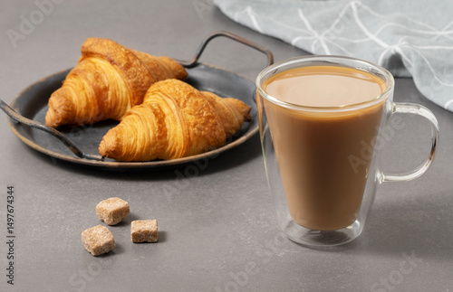 Freshly brewed coffee served with flaky croissants on a gray table with rustic tray and sugar cubes
