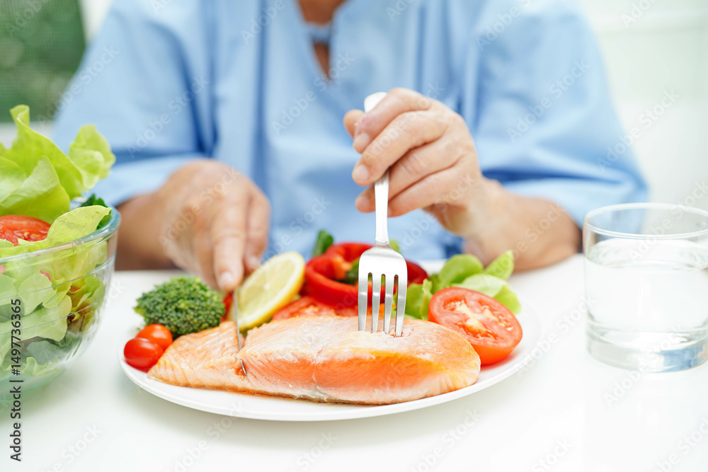 Asian elderly woman patient eating salmon stake and vegetable salad for healthy food in hospital. Asian elderly woman patient eating salmon stake and vegetable salad for healthy food in hospital.