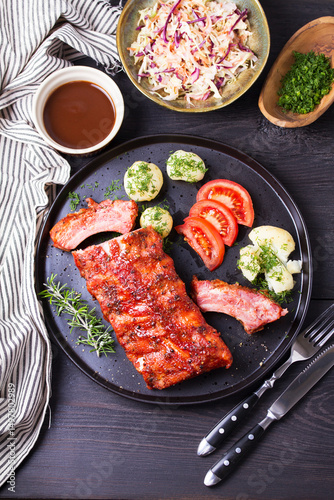Barbecue grilled pork ribs with boiled potatoes and fresh vegetables, black background. High angle view