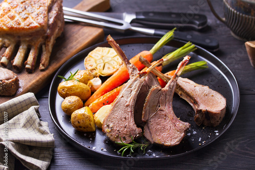Lamb chops with carrots and potatoes, black background. Roasted rack of lamb