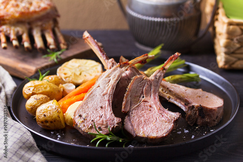 Lamb chops with carrots and potatoes, black background. Roasted rack of lamb