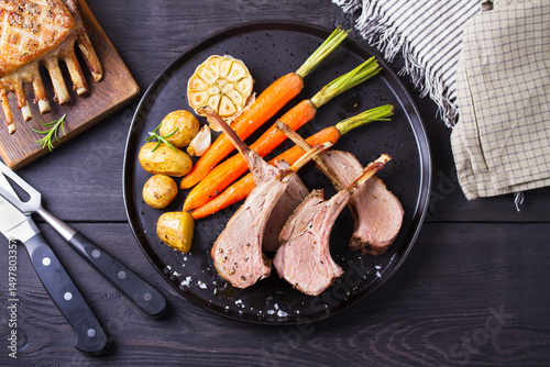 Lamb chops with carrots and potatoes, black background. Roasted rack of lamb. High angle view
