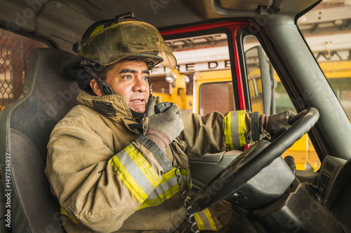 Firefighter driving a truck and talking on the radio to respond to a fire.