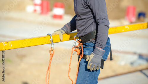 A worker in safety gear holds onto a yellow beam with safety ropes, emphasizing construction safety and rigging practices on a job site