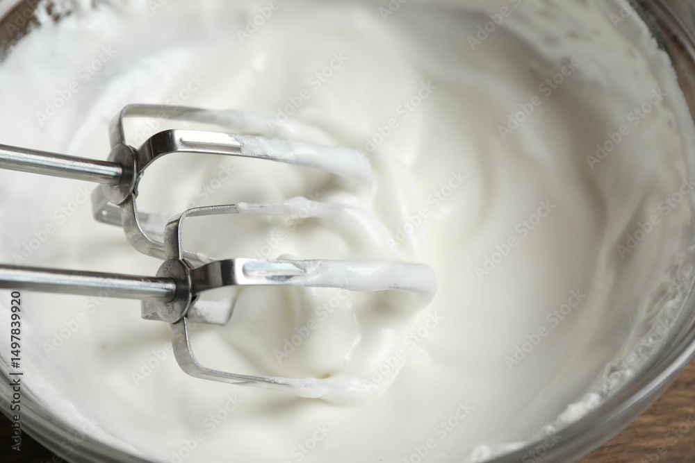 Fototapeta premium Hand mixer with whisks and bowl of whipped cream on table, closeup