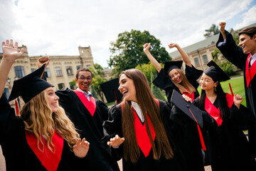 Joyful graduates celebrate outside university, wearing caps and gowns, with excitement. Friends cheer together in urban setting.
