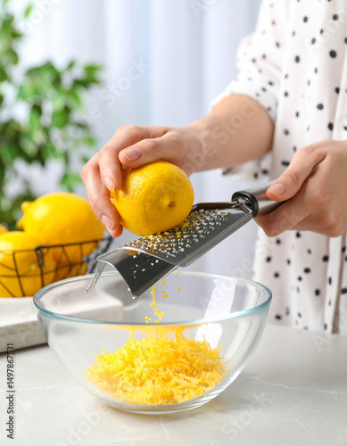 Bright yellow lemon zest is being grated with a zester over a clear glass bowl, adding citrus flavor.