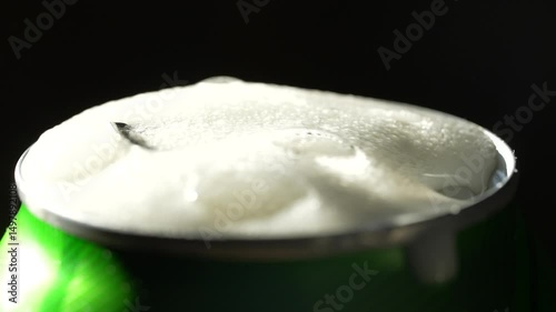 Opening metal beer can with foam, close up. Hand open a can of beer, black background