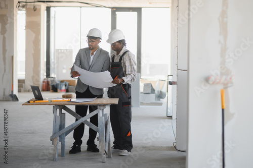 Architect and builder examining blueprints on construction site