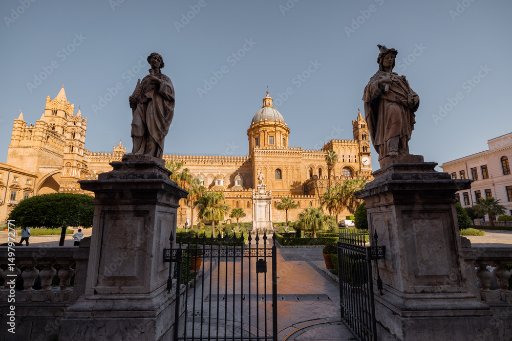 Obraz premium The grand entrance of Palermo Cathedral framed by Moorish arches and lush palm trees, bathed in the golden evening light. A timeless blend of cultures in the heart of Sicily