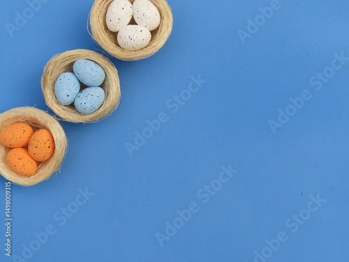 Straw nests with decorated Easter egss on blue background. Easter background. Bird nests crafts.  photo