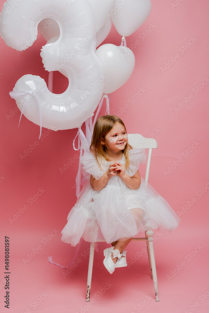 Fototapeta premium little girl with balloons and the number three on a pink background celebrates her birthday in the studio