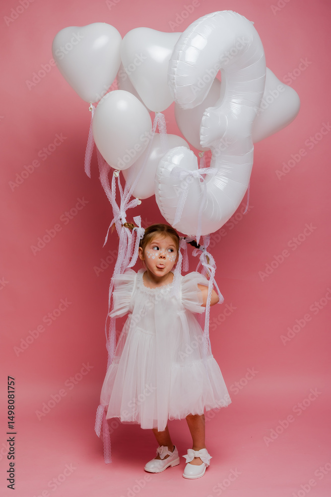 Fototapeta premium little girl with balloons and the number three on a pink background celebrates her birthday in the studio