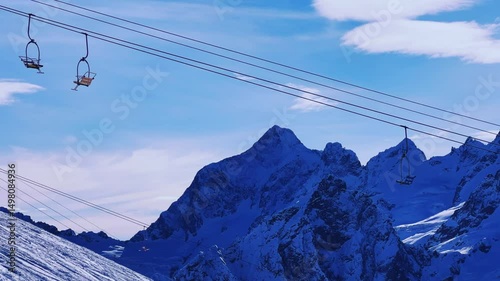 View of the cable car against the backdrop of Dombay glaciers and mountain peaks in the rays of the winter sun.Panorama of the snow-covered Caucasus Mountains in sunny weather. Ski resort in Russia.4К
