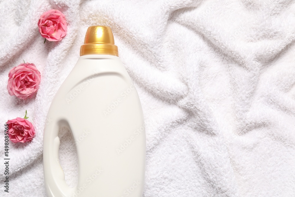 Bottle of fabric softener and flowers on terry towel, flat lay. Space for text Bottle of fabric softener and flowers on terry towel, flat lay. Space for text