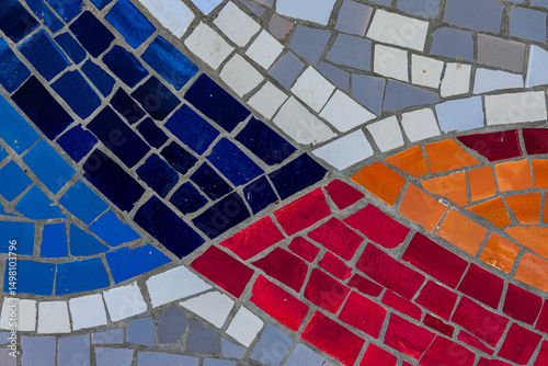 Close-up of a vibrant mosaic featuring curved bands of red, blue, orange, white, and gray tiles arranged in an abstract pattern.