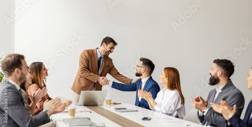 Friendly executive shaking hands and congratulating his associate for business success while team clapping hands.