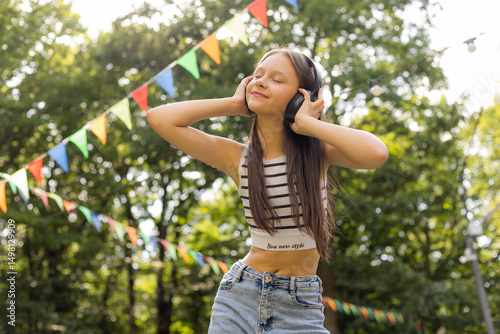Happy teenage girl listens to music with headphones in summer park