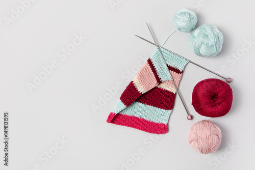 Brown beige vinous and turquoise piece of striped knitting with knitting needles and balls of thread on gray background. Homemade needlework and knitting of warm, clothes and toys. Concept creativity