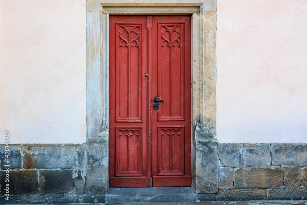 Fototapeta premium Rustic red wooden door with stone surround on weathered wall
