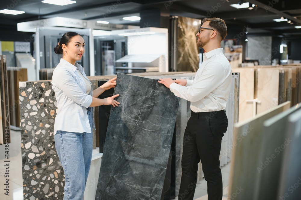 Fototapeta premium Shop assistant showing ceramic tile to woman in hardware store