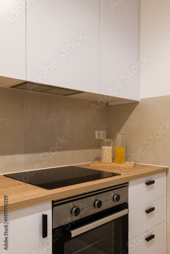 Minimalist kitchen close-up of cooktop and oven with wood countertop  white cabinets and backsplash