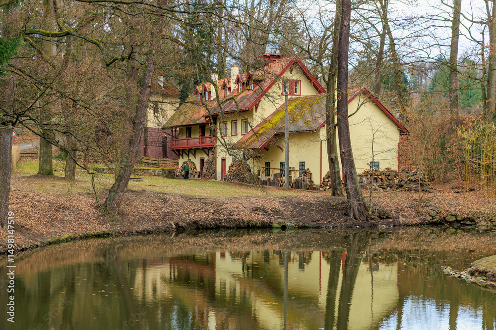 Obraz premium Historic rustic house by tranquil pond in serene forest setting